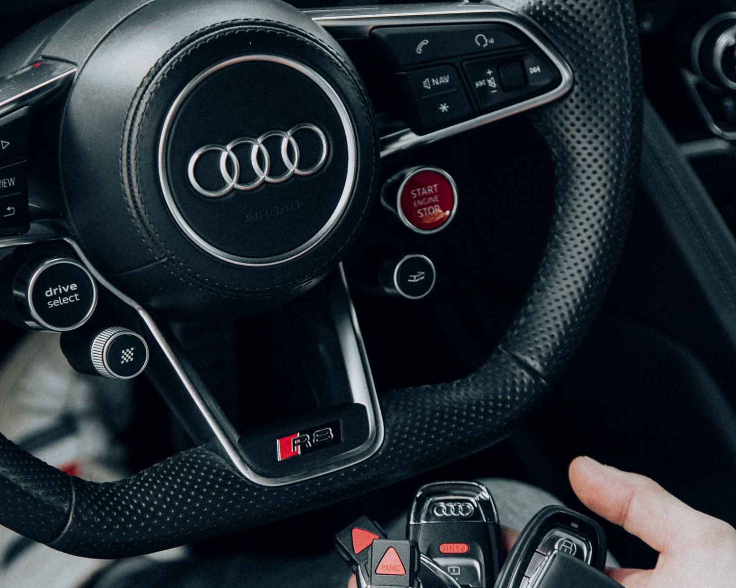 Audi R8 steering wheel with start-stop button and Audi remote car keys held inside the vehicle.
