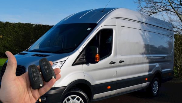 Hand holding two programmed van keys in front of a commercial vehicle