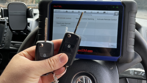 Hand holding two car keys inside a Volkswagen with a diagnostic tool displayed for remote key programming